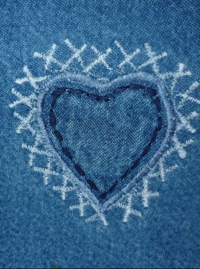 Dibujo del contorno de un corazón azul rey sobre un fondo azul más claro y taches pequeños en blanco alrededor del corazón en una textura que simula mezclilla